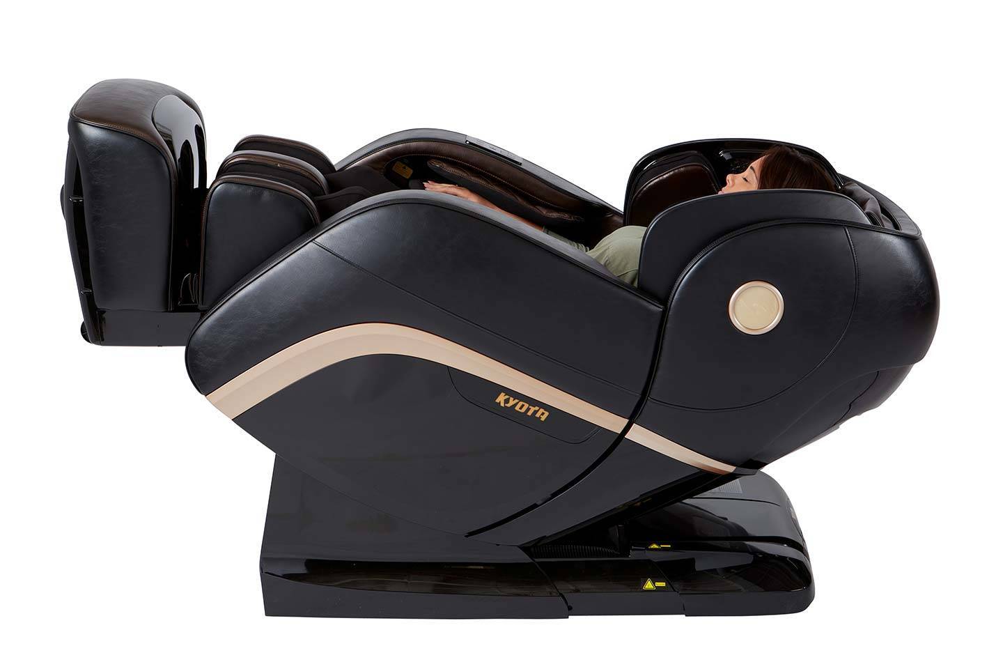 A person is relaxing in a high-end, black massage chair with a logo on the headrest, reclined in a zero-gravity position for optimal comfort. The design of the chair envelops the user's body, suggesting a deep, therapeutic massage experience.