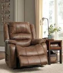 Partially reclined recliner with brown faux leather upholstery next to a side table, on top of an off-white rug.