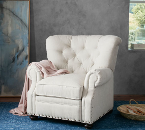 Recliner with ivory fabric upholstery, tufted back and nailhead accents in upright position. A pale pink blanket is draped over the arm of the recliner, and it sits in a room with gray walls and ocean blue carpeting.