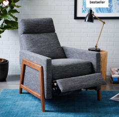 Mid-century modern-style recliner with dark gray woven upholstery and wood arms in a room with white brick walls and an aqua-colored rug.