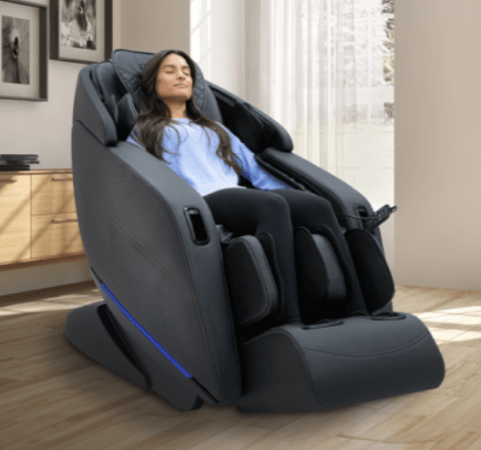 A woman relaxes in a black Kyota Yugana massage chair, place in a brightly-lit room.